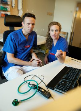 två forskare, en kvinna och en man, i blå vårdkläder sitter och tittar på forskningsresultat.