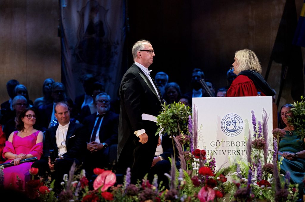 Bengt Nellgård står upp i frack och pratar med rektor Eva Wiberg på en scen som är omringad av blommor